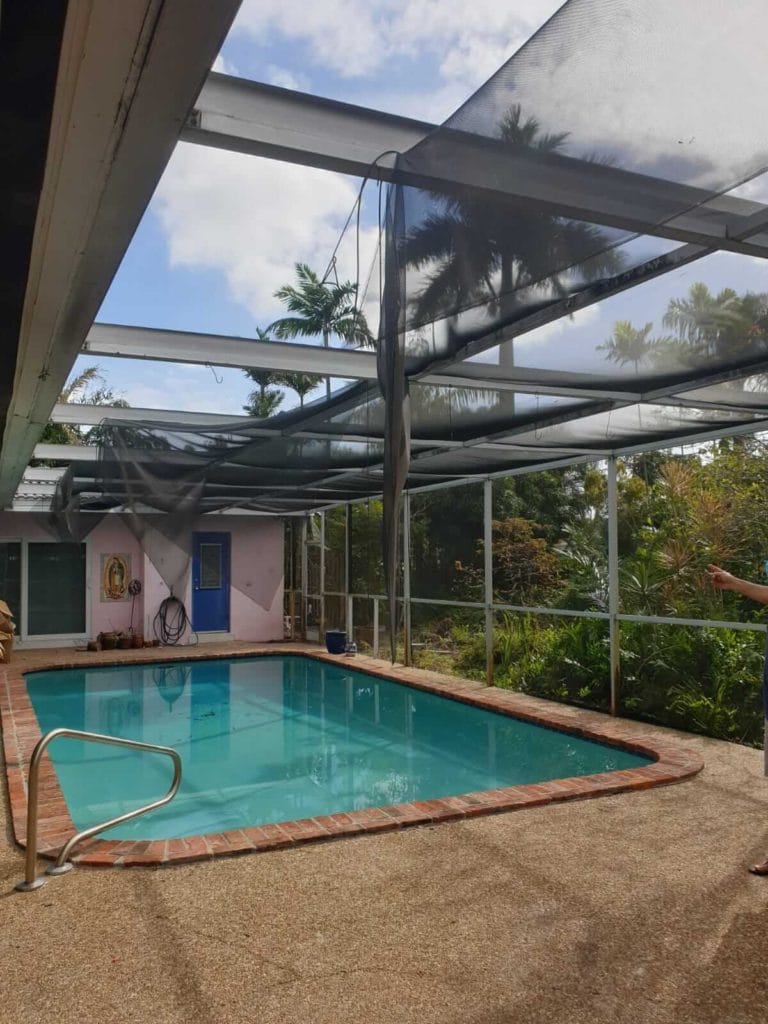 Torn screen panels over pool enclosure showing structural damage.